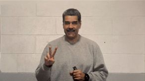 Maduro viste un chándal gris mientras hace el gesto de la paz con las manos.